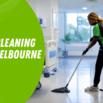 Healthcare Cleaning Standards Melbourne | Spiffy Clean - Commercial & Office Cleaning Services Hospital cleaner mops a bright hallway while wearing a green-and-black uniform; blue 'Patient Rooms' sign visible in the doorway.